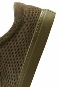 Olivgrüner Sneaker mit einem Obermaterial aus Wildleder und Mesh, das mit Perforationen versehen ist, verstärkter Zehenkappe und einer Gummisohle, die Atmungsaktivität und Langlebigkeit bietet.