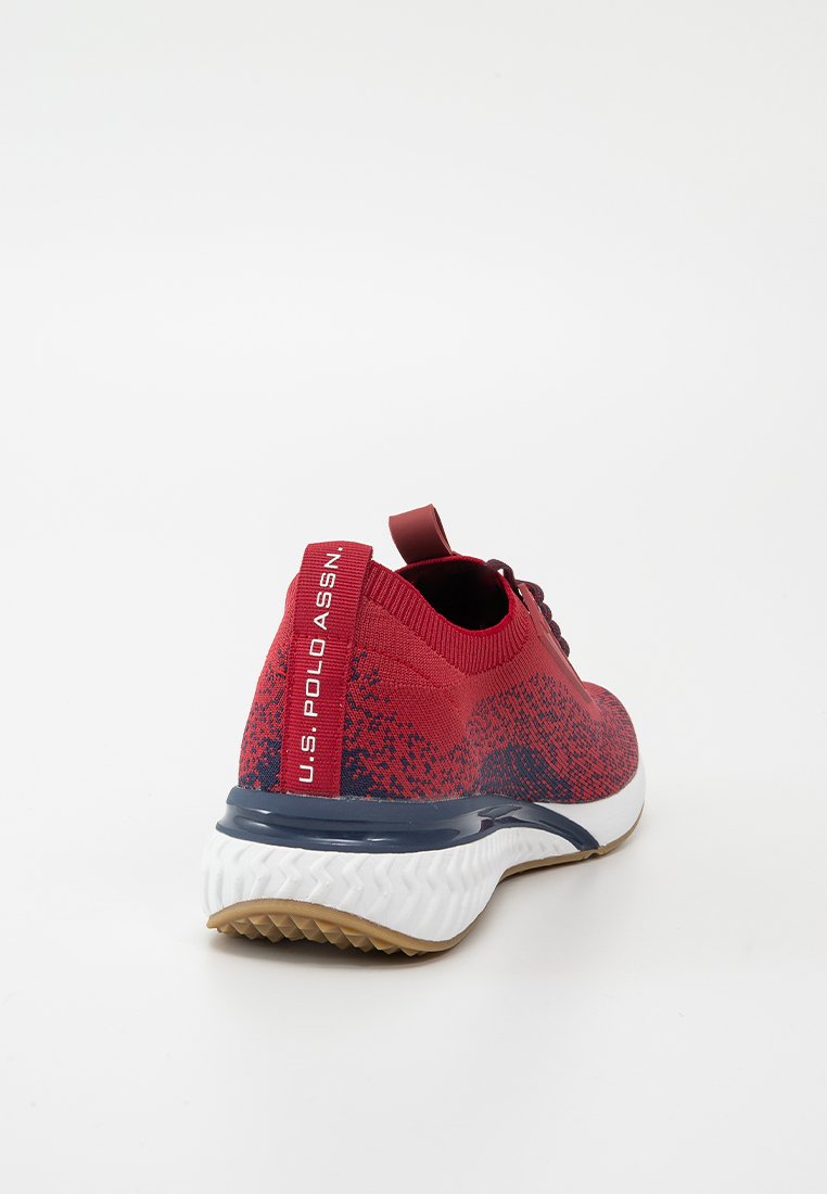 Chaussure de sport rouge avec une texture en tricot, accents bleu marine et semelle blanche. Présente un logo sur le talon et un col rembourré.