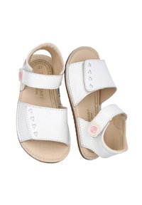 Sandalias blancas para bebé hechas de cuero texturizado, que cuentan con dos correas ajustables con cierres de Velcro y pequeños recortes en forma de corazón en el lateral.