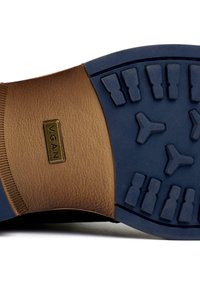 Brown vegan leather sole with a blue rubber bottom. Features textured patterns and a gold emblem reading "V.GAN" near the heel.