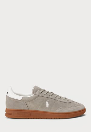 Jasnoszare zamszowe niskie sneakersy z białą łatką na pięcie, brązową gumową podeszwą, sznurowadłami i białym wyszywanym logo Polo Ralph Lauren po boku.