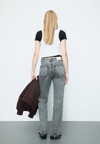 Mustat ja valkoiset kuvioidut korkeavyötäröiset farkut suoran lahkeen kanssa, yhdistettynä lyhytlahkeiseen mustan ja valkoisen yläosaan, pitäen ruskeaa bomber-takkia.