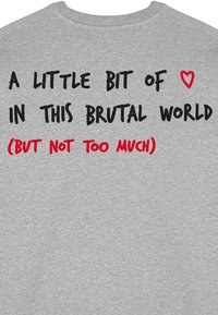 Grijze sweatshirt met gedurfde zwarte en rode tekst: "EEN BEETJE ♥ IN DEZE BRUTE WERELD (MAAR NIET TE VEEL)." Zacht, textuurstof.