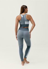 Szary zestaw sportowy składający się z krótkiego topu na ramiączkach o konstrukcji racerback oraz legginsów z wysokim stanem, oba z kolorowymi panelami i teksturowanym materiałem.