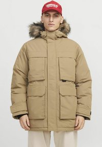 Béžová zateplená parka s kapucí a umělým kožíškem. Obsahuje několik předních kapes a zapínání na zip s nastavitelnými manžetami.