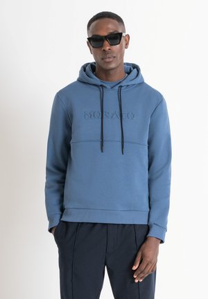 Sudadera azul con logotipo texturizado "MORATO", con cordones ajustables, puños y dobladillo acanalados. Llevada con pantalones oscuros, de corte relajado.