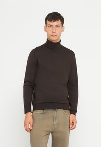 Donkerbruin coltrui van zachte stof, met een aansluitend ontwerp en geribde manchetten. Gecombineerd met lichte jeans.