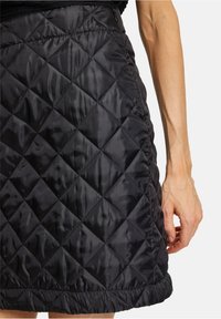 Svart quiltad kjol med en glänsande, vadderad textur, med diamantmönster och resårmidja, förhöjd av en rynkad nederkant.