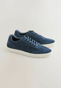 Marineblå ruskindssneakers med tekstureret overdel, hvide gummisåler og flade snørebånd. Har minimal syning og et klassisk lavprofildesign.