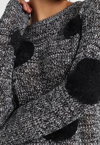 Pull en tricot noir et blanc avec de grands pois noirs duveteux, un design ample et des poignets côtelés. Texture douce partout.