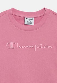 Ροζ βαμβακερό t-shirt με στρογγυλή λαιμόκοψη. Φέρει κεντητό λογότυπο "Champion" σε λίγο πιο σκουρό ροζ. Μαλακή υφή, καθημερινό σχέδιο.