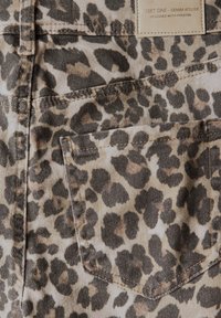 Tessuto in denim con stampa leopardata, caratterizzato da macchie color sabbia e marrone scuro, con cuciture visibili e una tasca sul retro sul lato destro.