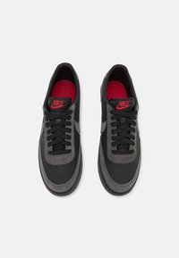 Črne in sive Nike športne copate iz usnja in semiša, okrogla konica, teksturirani detajli, črne vezalke in rdeča notranjost.