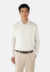 Vevd langermet skjorte med lys beige og hvite vertikale striper. Har spiss krage og knapper, kombinert med lyse beige bukser og et strukturert mørkt belte.