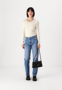 Suéter de punto blanco con escote redondo, combinado con jeans de tiro alto azul claro y zapatos de cuero negros. Lleva un pequeño bolso negro.