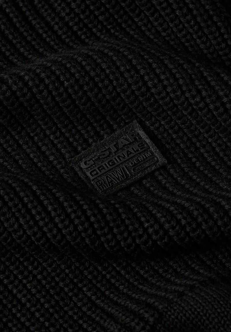 Gorro de punto negro con un patrón texturizado y una etiqueta rectangular de tela negra con texto en relieve para G-Star RAW.