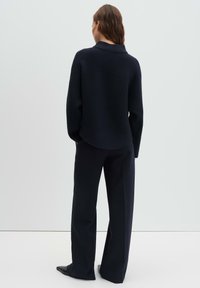 Maglione in maglia a coste blu navy con collo alto, abbinato a pantaloni sartoriali blu navy. L'outfit presenta una vestibilità comoda e una texture sottile.