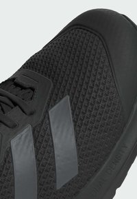 Baskets de sport noires avec une tige en maille texturée, un embout renforcé et des rayures grises. Comprend un amorti à double densité.