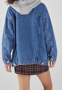 Blauwe oversized spijkerjas met grijze capuchon, voorzien van knoopsluiting, gestikte details, en een geruite minirok.