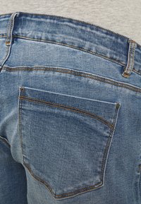 Light blue denim jeans with a standard back pocket, visible stitching accents in contrasting orange, and a slightly faded texture.