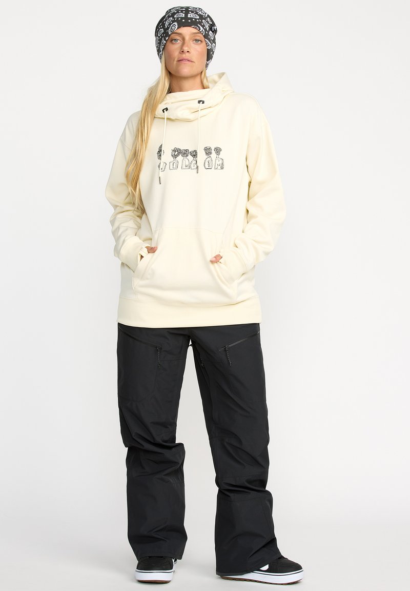 Sweatshirt crème avec un design graphique noir, poches avant et capuche avec cordon de serrage ; associé à un pantalon de neige noir avec poches zippées.