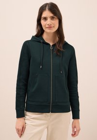 Felpa zip con cappuccio di colore verde scuro, con un cappuccio regolabile tramite lacci, due tasche frontali, polsini a coste e un tessuto morbido e testurizzato.