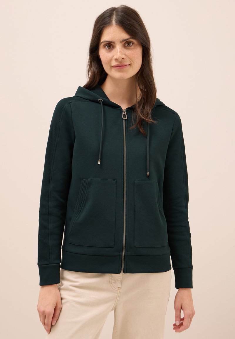 Sudadera con cremallera de color verde oscuro, con capucha ajustable, dos bolsillos frontales, puños de canalé y una tela suave y texturizada.