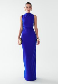 Modra obleka dolžine do tal z visokim vratnim izrezom in brez rokavov. Gladek tekstilen material z naborki v predelu pasu. Zlati dodatki.