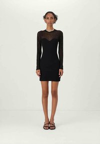 Black long-sleeve mini dress with sheer material featuring a sweetheart neckline and scattered embellishments. Form-fitting silhouette.