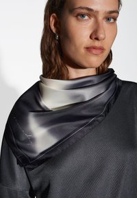 Fazzoletto di seta nera con sfumature che vanno da crema a grigio scuro, caratterizzato da un sottile contorno blu e dettagli in scrittura lungo il bordo.