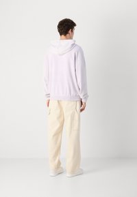 Hanorac violet deschis cu șnur, cu talie strânsă, asortat cu pantaloni cargo bej cu buzunare laterale. Textură fină, croi lejer.