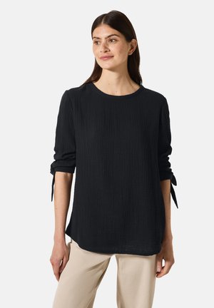 Zwart, met structuur, lang mouw shirt met een ronde hals en gestrikte manchetten, gecombineerd met lichtbeige broeken. Eenvoudig, relaxed fit ontwerp.