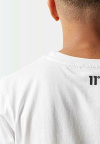 Camiseta de algodón blanca con cuello redondo, que presenta un pequeño logotipo negro "11°" en la parte de atrás, cerca del cuello. Textura suave, corte relajado.