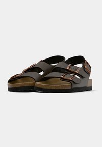 Brown sandals with two adjustable straps, copper-colored buckles, and a textured cork sole. Open-toe design with a contoured footbed.