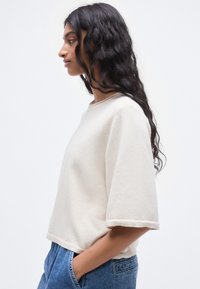 Πουλόβερ σε κρεμ απόχρωση με κοντά μανίκια, στρογγυλή λαιμόκοψη και άνετη εφαρμογή. Μαλακή υφή με ελάχιστες ραφές. Φορεμένο με τζιν παντελόνι.