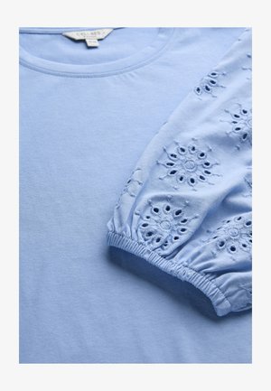 Lichtblauw shirt met lange mouwen en elastische manchetten, voorzien van geborduurde bloemmotieven met uitsnijdingen.