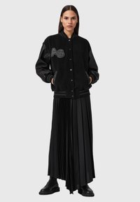 Giacca da varsity nera con corpo in suede, maniche in pelle e polsini a coste. Caratterizzata da un logo ricamato "AS". Abbinata a una gonna nera plissettata.