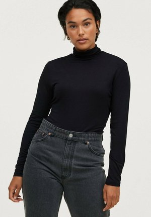 Black long-sleeve turtleneck top made of smooth fabric, paired with high-waisted dark gray jeans featuring copper-toned hardware.
