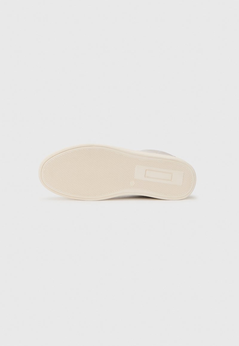 Semelle d'une basket, présentant une surface en caoutchouc texturé beige, avec un design plat et un branding subtil en relief.