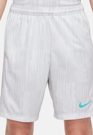 Białe spodenki sportowe z powtarzającym się subtelnym wzorem tekstu "NIKE" oraz turkusowym logo Nike w kształcie łyżwy w pobliżu lewego brzegu, noszone przez osobę.