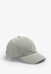 Hellgraue Kappe aus weichem Stoff, mit einem gebogenen Schirm und einem kleinen gelben Schädel-Logo auf der Vorderseite. Verstellbarer Riemen auf der Rückseite.