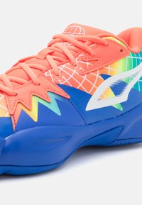 Zapatilla colorida que presenta una mezcla de materiales en coral, azul y verde, un diseño texturizado y un patrón distintivo en la parte superior.