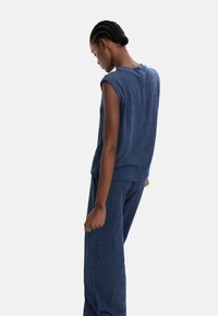 Niebieski, teksturowany, bezrękawnik i pasujące spodnie, o luźnym kroju i ryflowanej tkaninie, widok z boku z modelką patrzącą w dół.