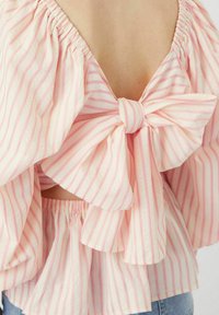 Blusa a righe in rosa pallido e bianco, con scollatura a V profonda sulla schiena, dettagliata con un grande fiocco e orlo elasticizzato per una vestibilità rilassata.