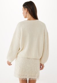 Ljusbeige, oversized stickad tröja med långa ärmar, avslappnad passform och en texturerad franskant, tillsammans med en matchande fransad minikjol.