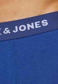 Blue cotton underwear waistband with "JACK & JONES" text in white on navy elastic band, showing part of a person's waist.