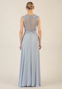 Helles blaues Kleid mit einem transparenten Netzrücken, der mit floraler Spitze verziert ist. Der Rock fließt bis zum Boden und hat einen sanften Schlitzausschnitt hinten für mehr Bewegungsfreiheit.