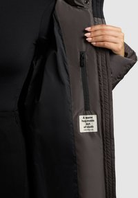 Gray insulated jacket with a ribbed interior, featuring a zipper pocket and a label stating, "A warm hug made out of cloth." Smooth texture.
