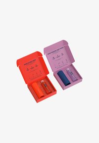 Zwei verpackte Körpersprays: das eine orange mit einer strukturierten zylindrischen Flasche, das andere lila mit einer glatten Flasche. Jede Box enthält Produktdetails.