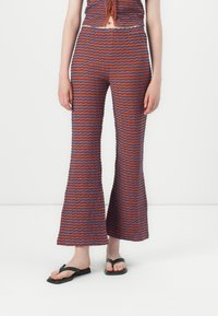 Uppvikta byxor i ett flerfärgat vågmönster, med orange och blå ränder. Tillverkade av texturerad tyg och kombinerat med svarta flip-flops.